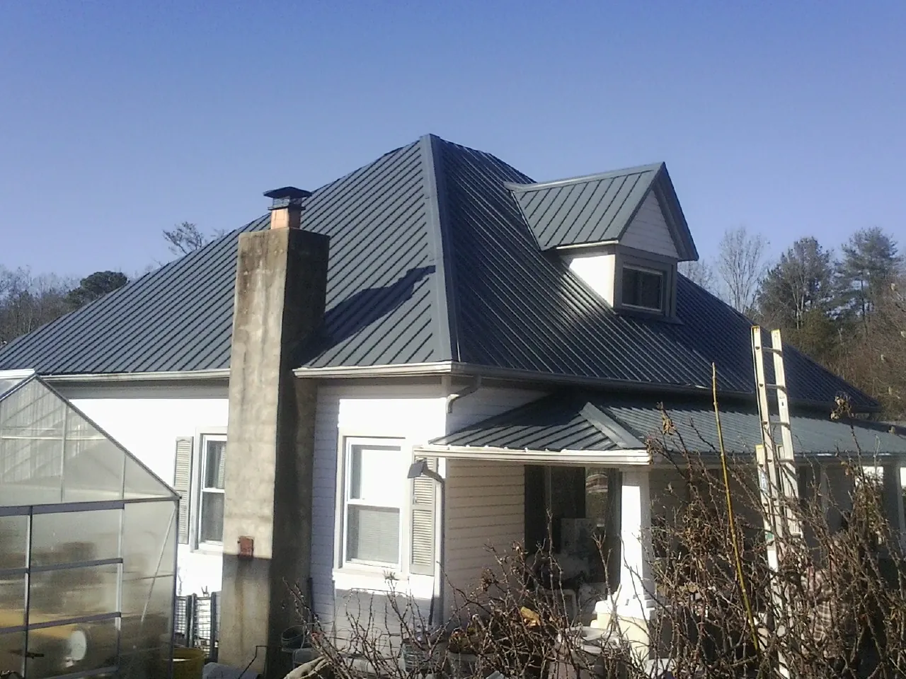 Dark blue standing seam metal roof on a white farmhouse with dormer — Slate & Tile Roof Repair by Roofing Brothers in Alto