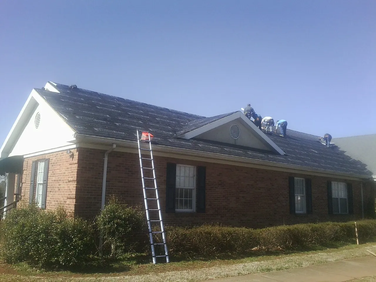 Crew tearing shingles off a brick ranch roof with a ladder set — Metal Roof Repair work by our crew in Alto