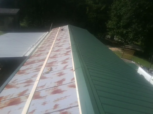 Old rusted panels beside newly installed green metal roofing — Wind Damage Roof Repair by Roofing Brothers in Alto
