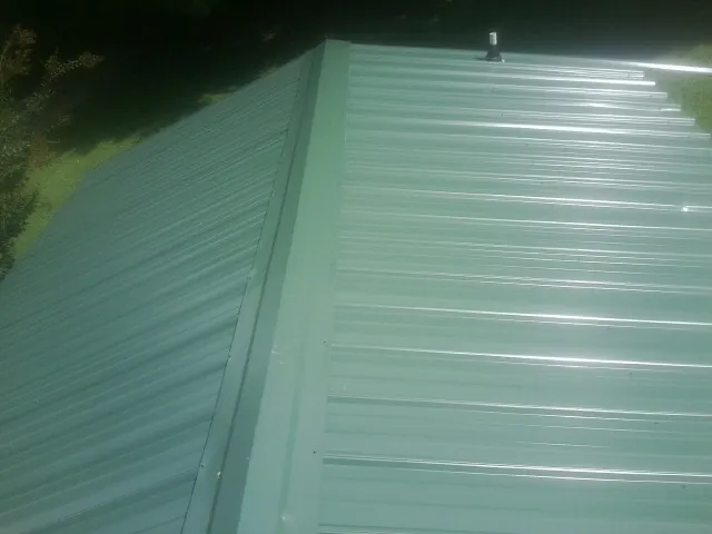 New green metal panels meeting at the ridge of a roof — Flat Roof Repair work by our crew in Alto