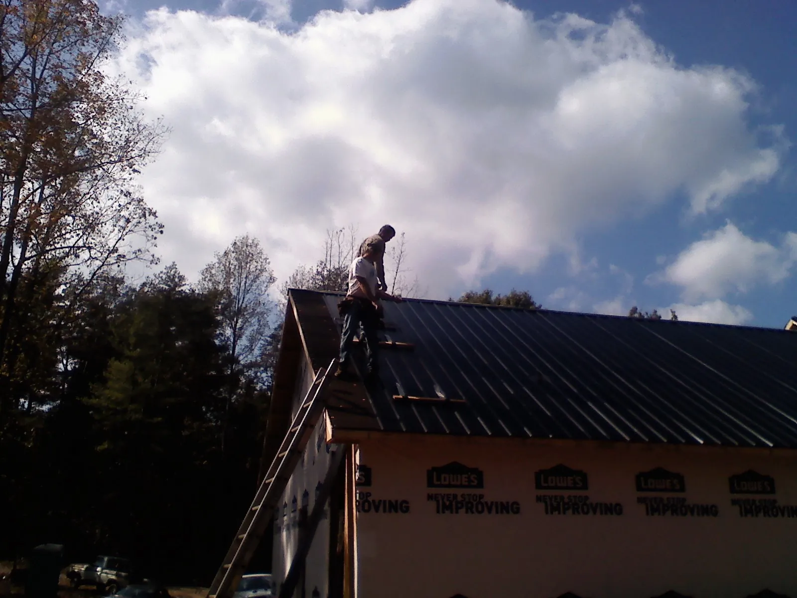 Roofer fastening dark metal panels high against a cloudy sky, from a Roof Inspection job in Alto