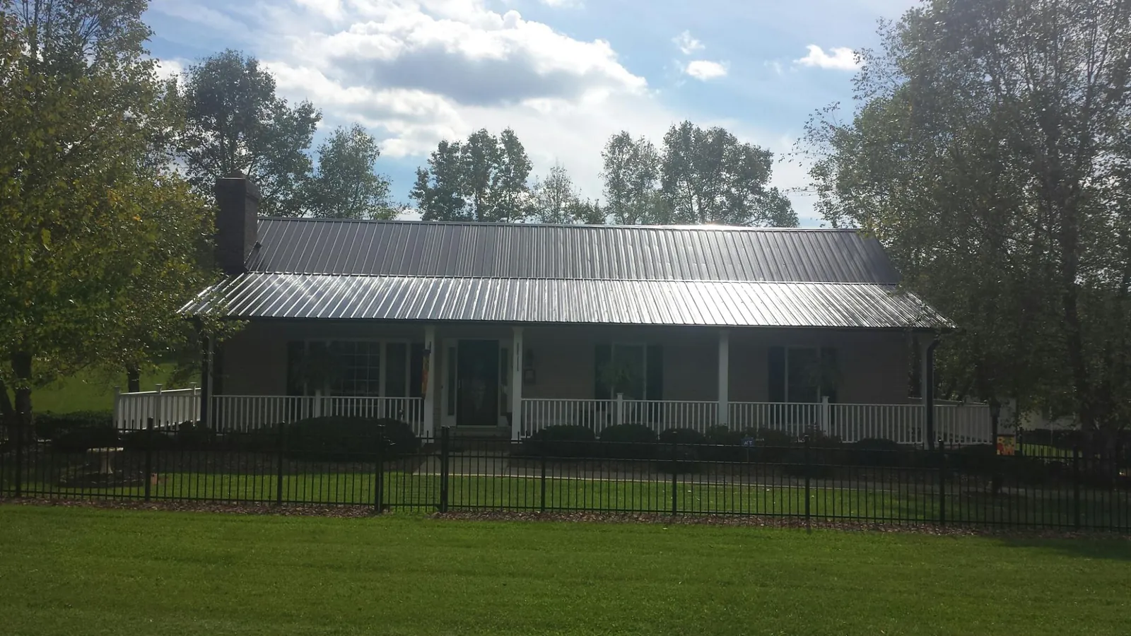 Gray metal roof on a brick ranch with a full width front porch — Gutter Guard Installation work by our crew in Alto