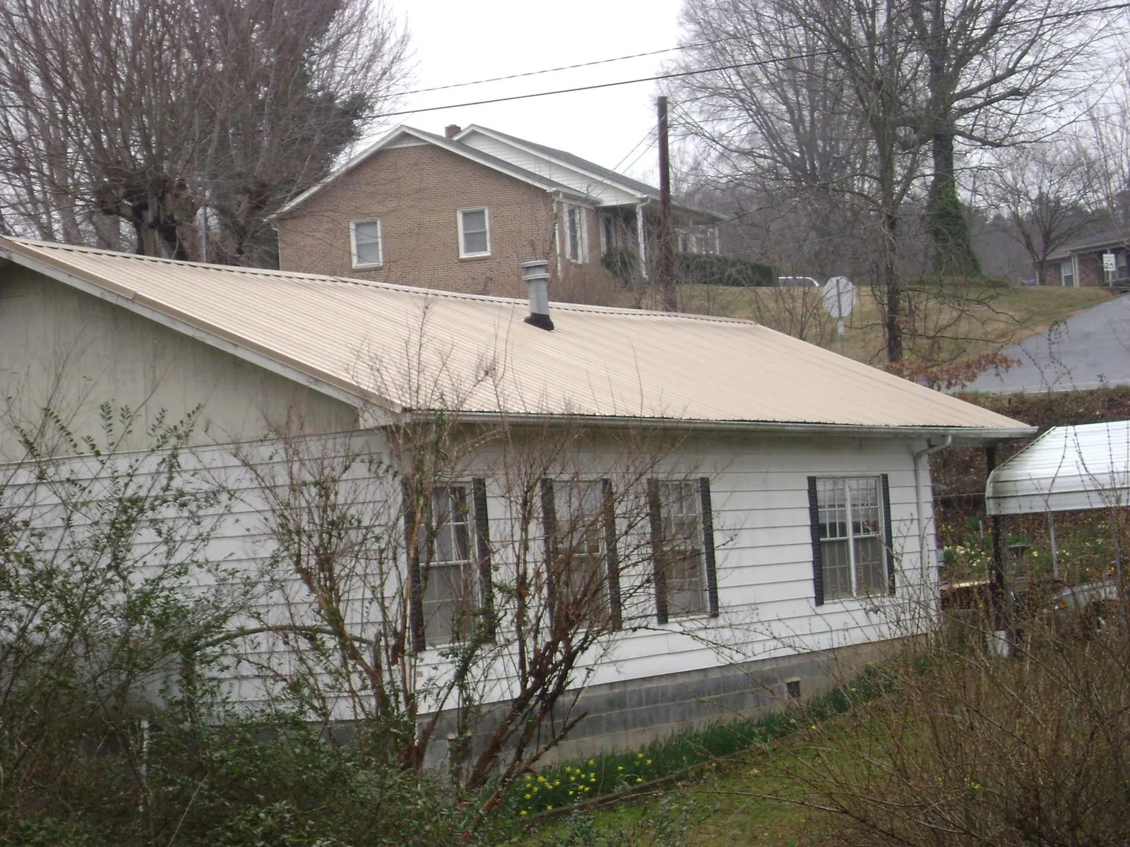 Tan metal roof on a white sided house set into a hillside — Commercial Roofing by Roofing Brothers in Alto