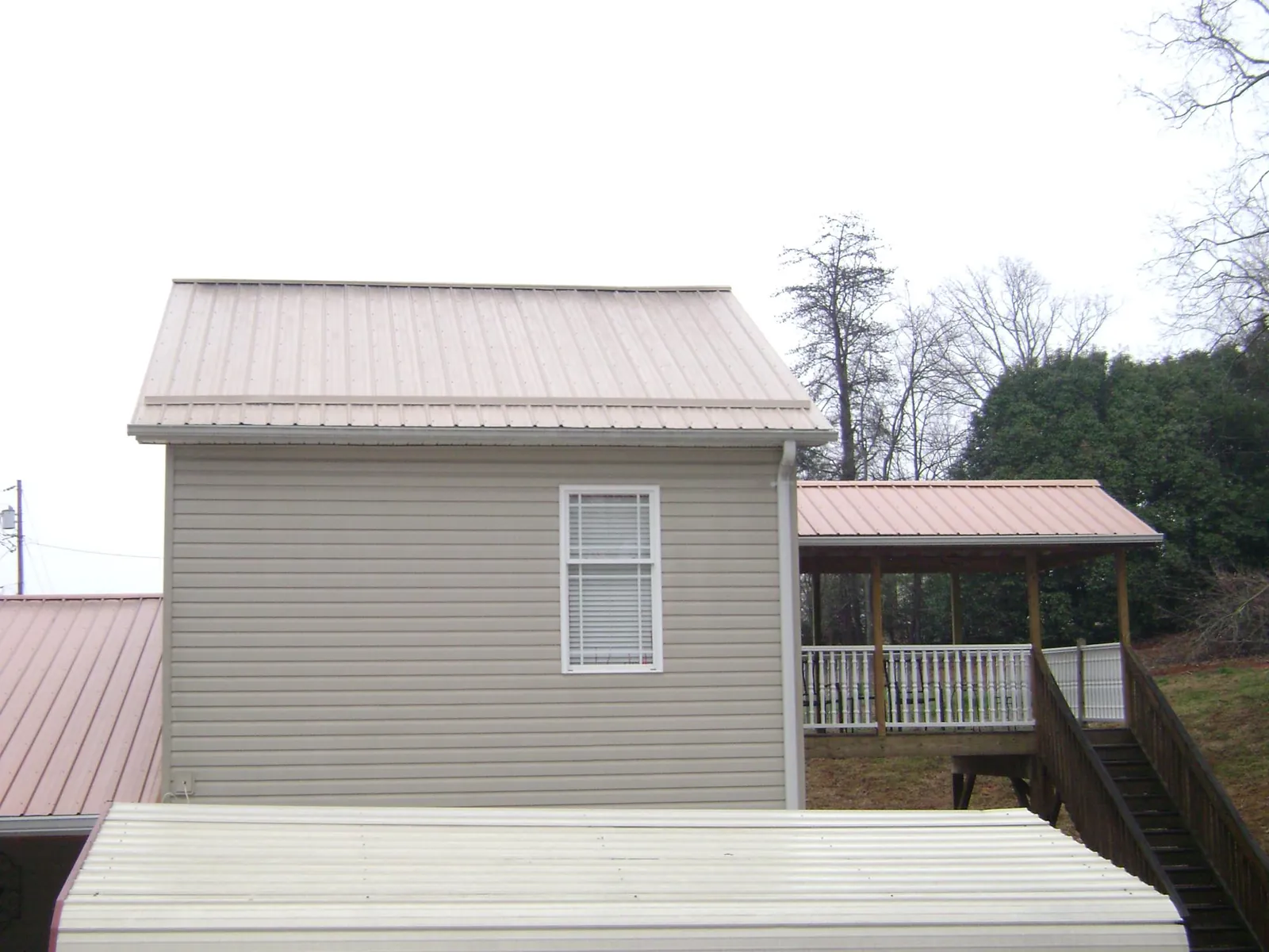 Tan metal roofs on a two story addition and attached porch, from a Roof Replacement job in Alto